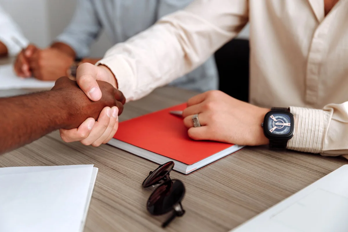 Two people shaking hands over documents at a closing table after a cash home sale