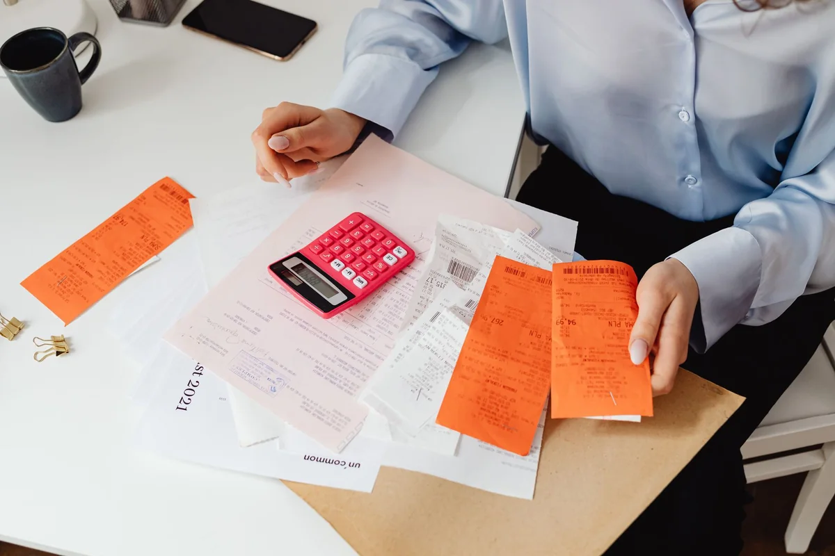 A person reviewing bills and paperwork with a calculator, the holding and closing costs cash home buyers subtract to calculate their offer