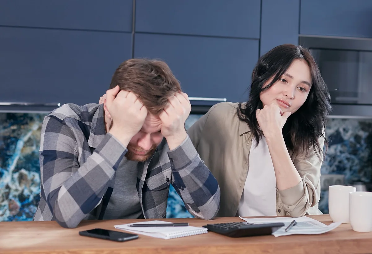 A person reviewing bills at a kitchen table, working out whether one income covers the mortgage