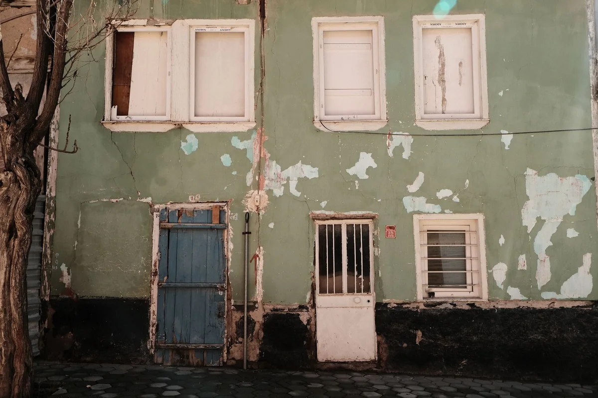 An old abandoned house with peeling paint and a boarded door that an owner still holds title to