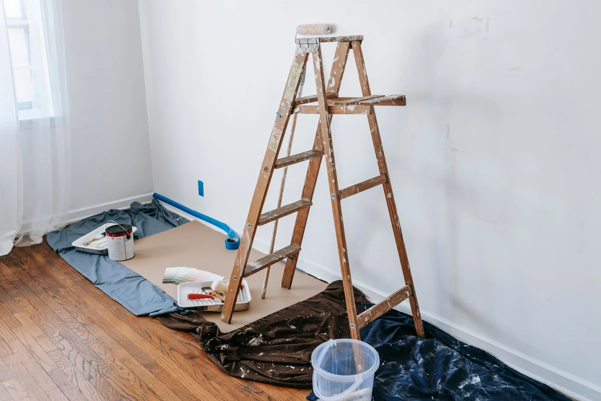 A stepladder and paint supplies in an empty room mid-renovation, weighing whether to finish before selling