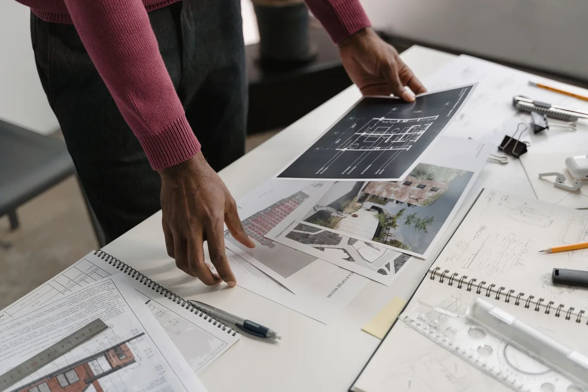 A person reviewing renovation plans and paperwork at a table, comparing options for selling a half-finished house