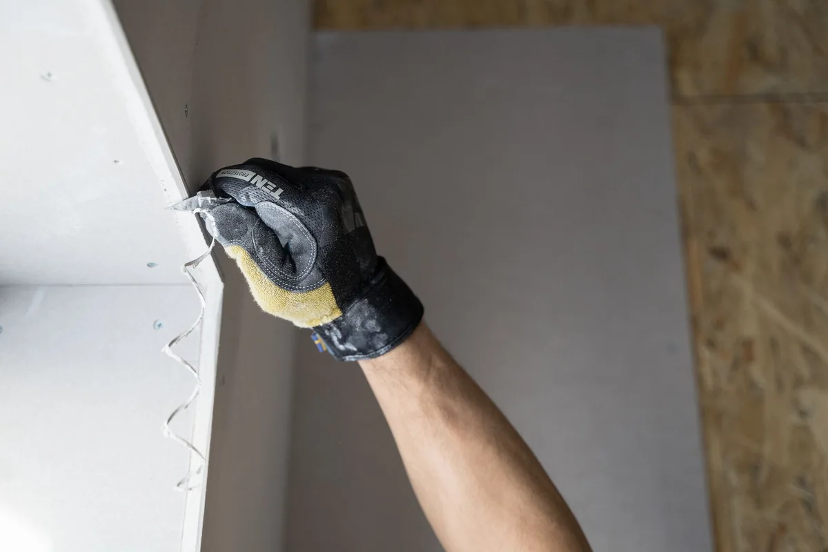 A worker in gloves repairing drywall damaged by water