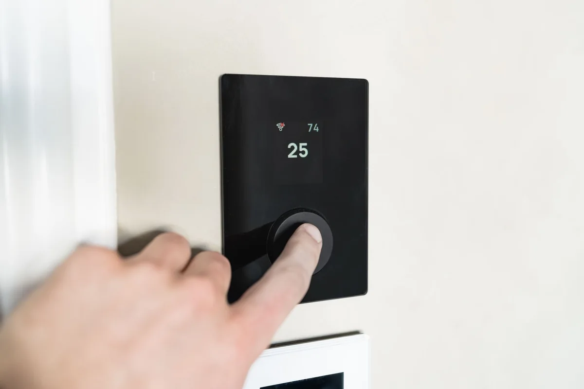 A hand adjusting a home thermostat in a cold house with a bad furnace