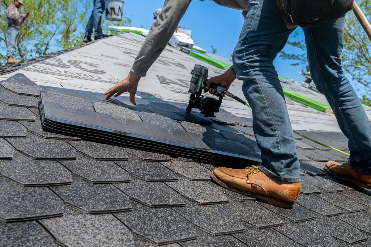 A roofer nailing down new asphalt shingles on a replacement roof