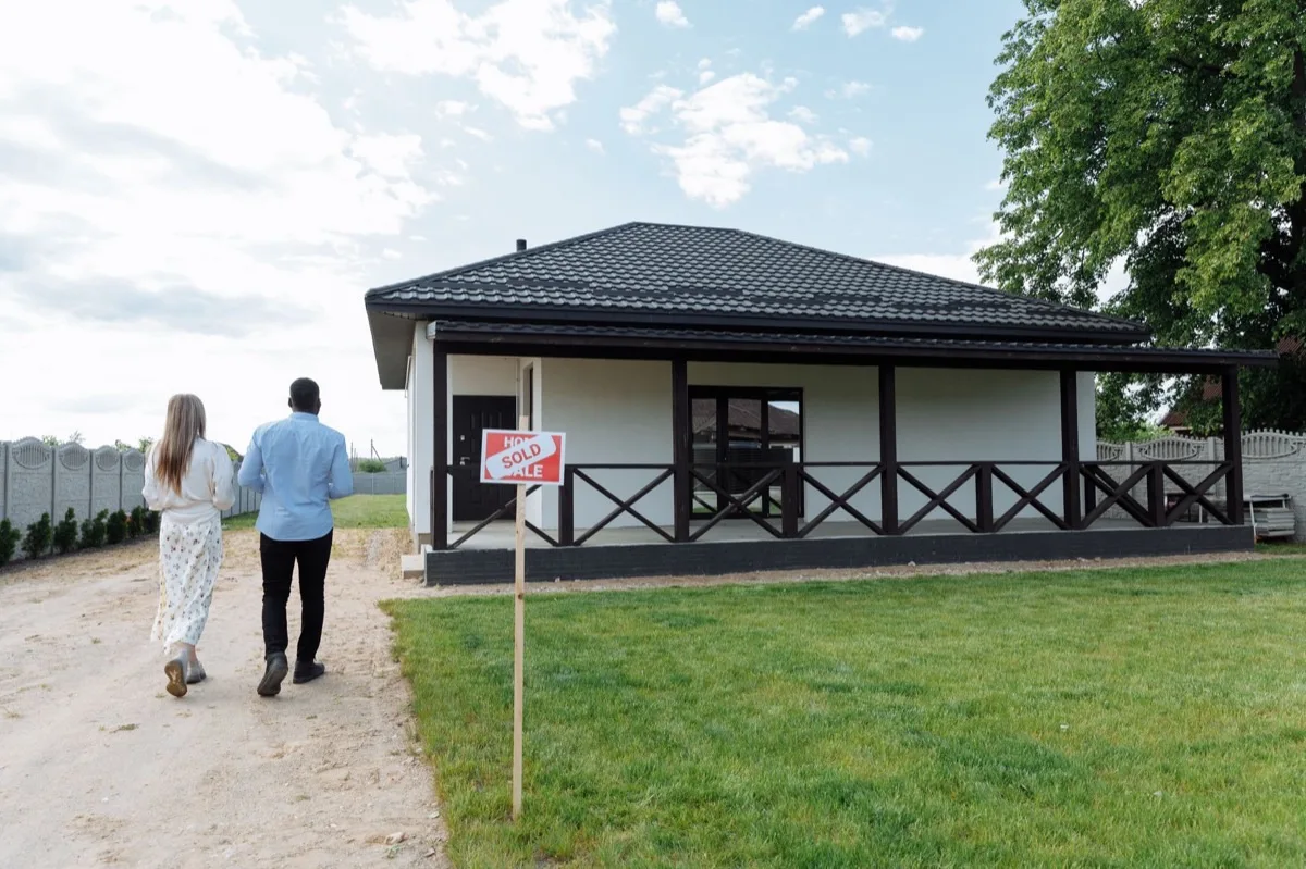 A couple walking toward a home with a sold sign, showing a house with radon still sold in Iowa