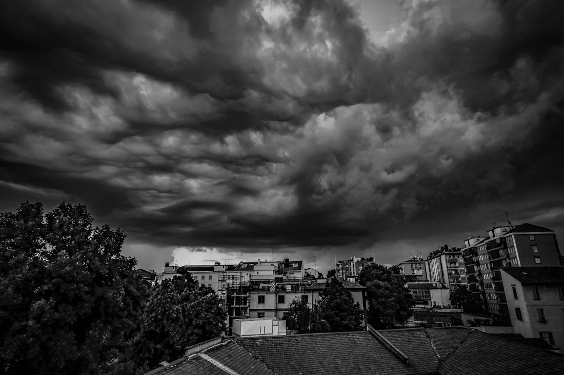 Dark storm clouds rolling over Iowa rooftops before selling a house with storm damage