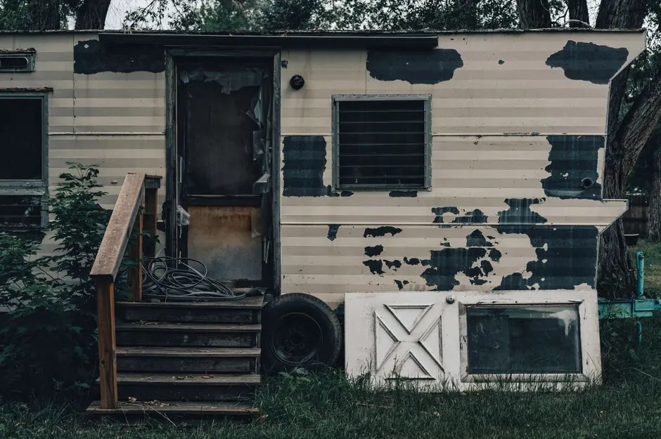 A weathered single-wide mobile home with peeling siding and wooden steps, the kind of place people picture when selling a mobile home in Iowa