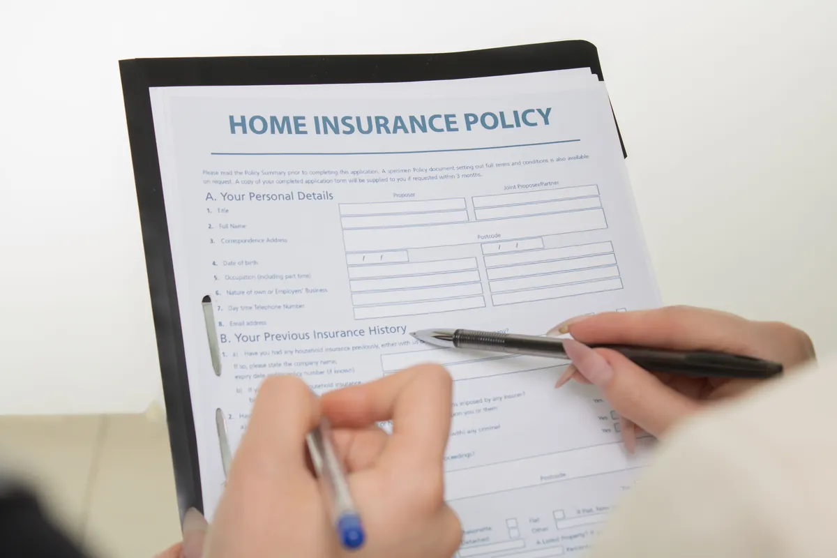 Hands filling out a home insurance policy document for a vacant house
