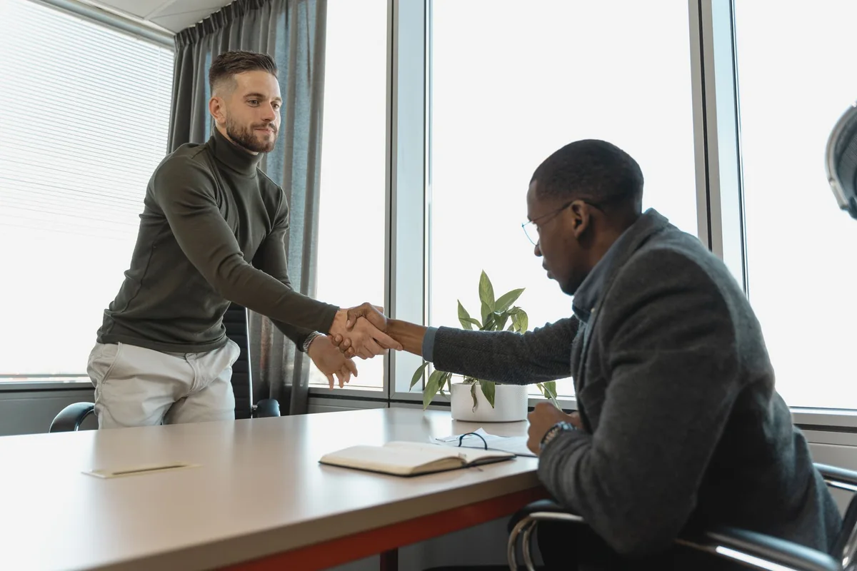 Two people shaking hands over a desk at a real closing, the transparent process a legitimate Iowa cash home buyer follows